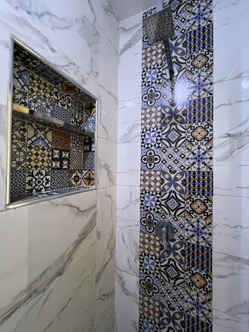 A bathroom with a tiled wall featuring a geometric pattern and a rectangular mirror with a gold frame.