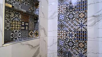 A bathroom with a tiled wall featuring a geometric pattern and a rectangular mirror with a gold frame.