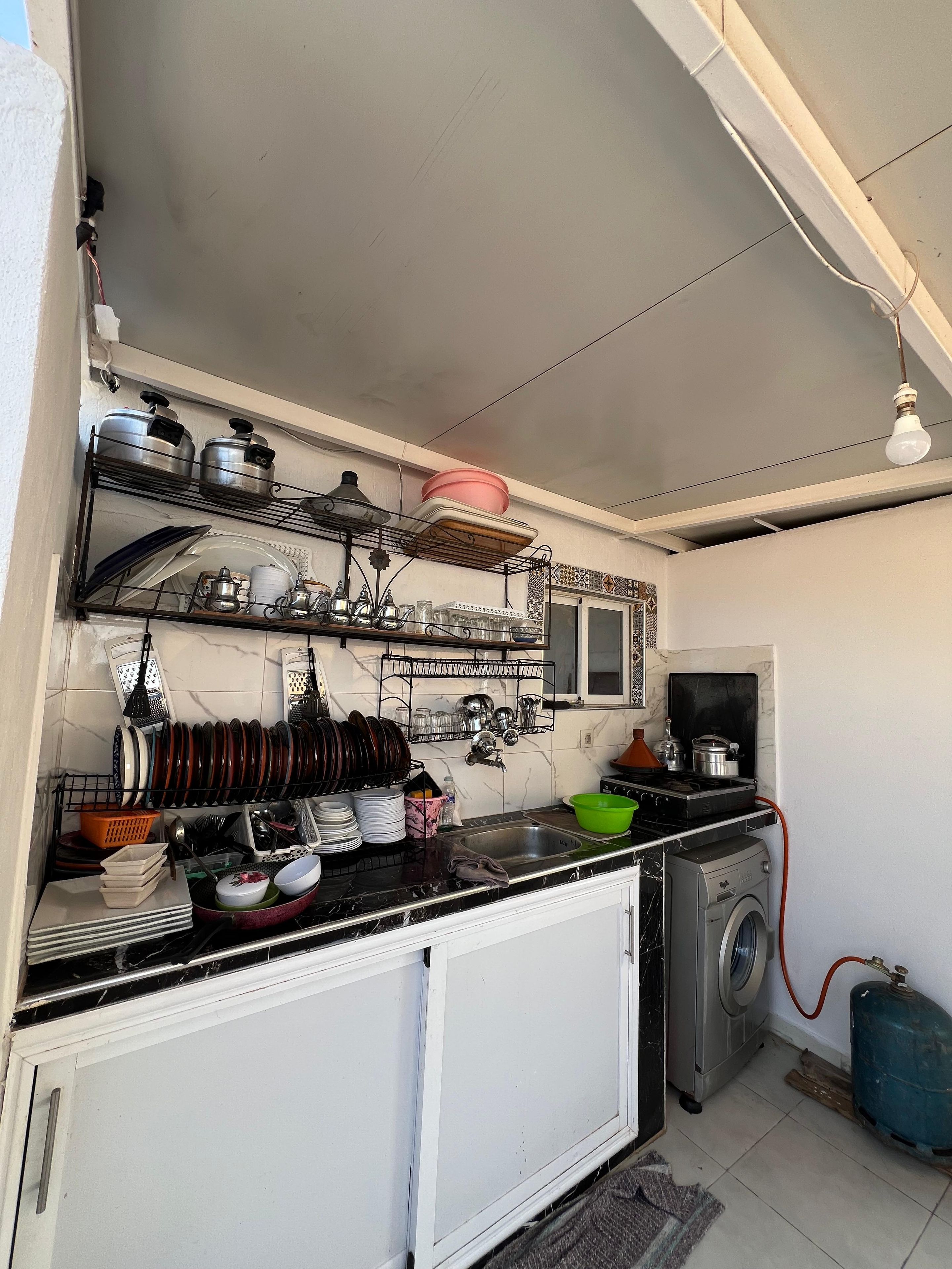 Une cuisine compacte équipée d’un lave-linge, d’une cuisinière à gaz et de divers ustensiles et articles de vaisselle.