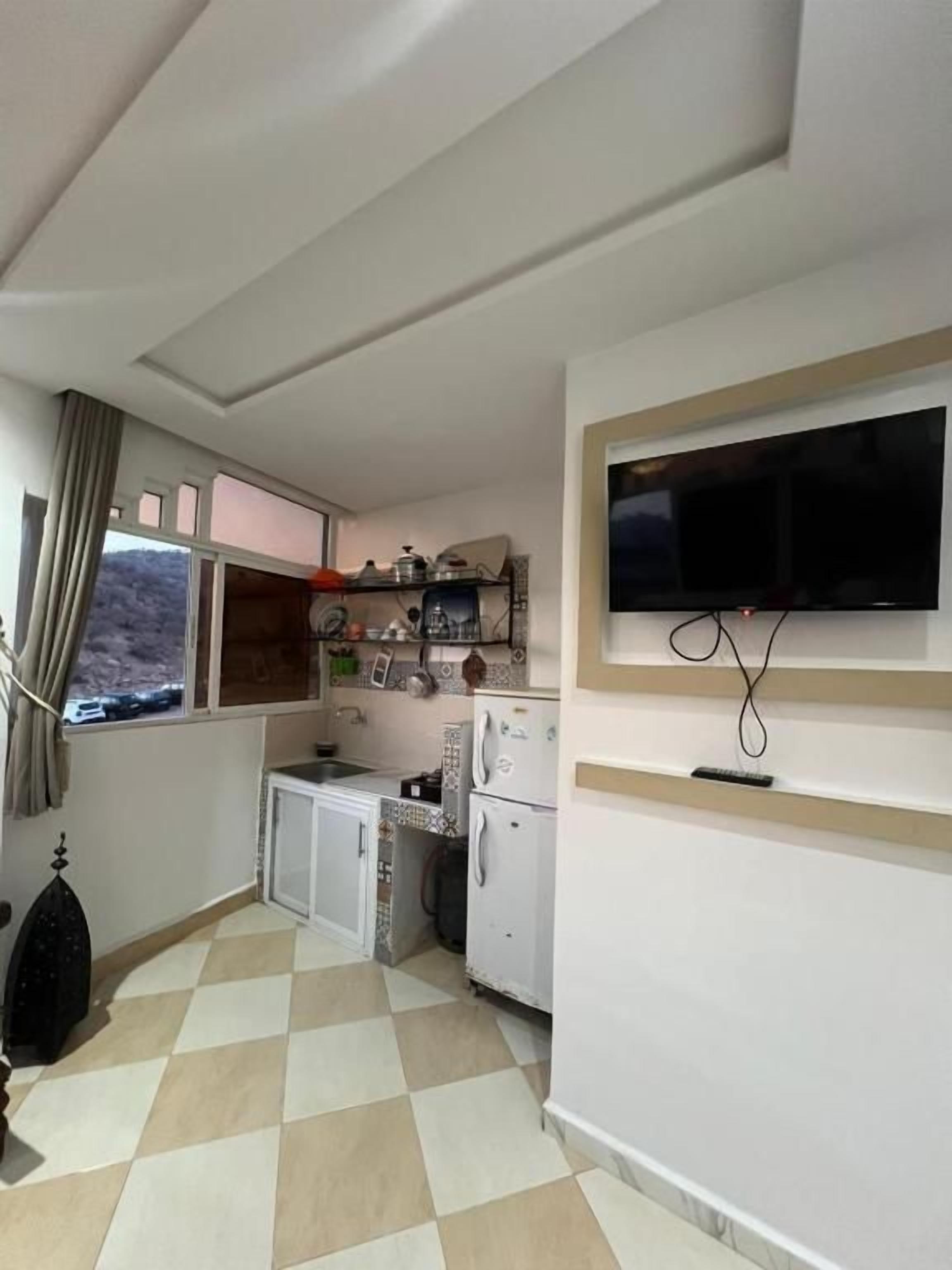 Una cocina compacta con ventana, un televisor de pantalla plana en la pared y un refrigerador pequeño.