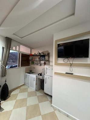 Een compacte keuken met een raam, een flatscreen televisie aan de wand en een kleine koelkast.