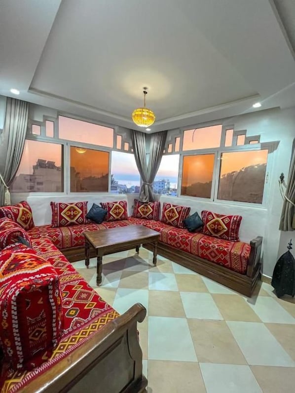 A room with a sofa set, a coffee table, and a view through large windows.