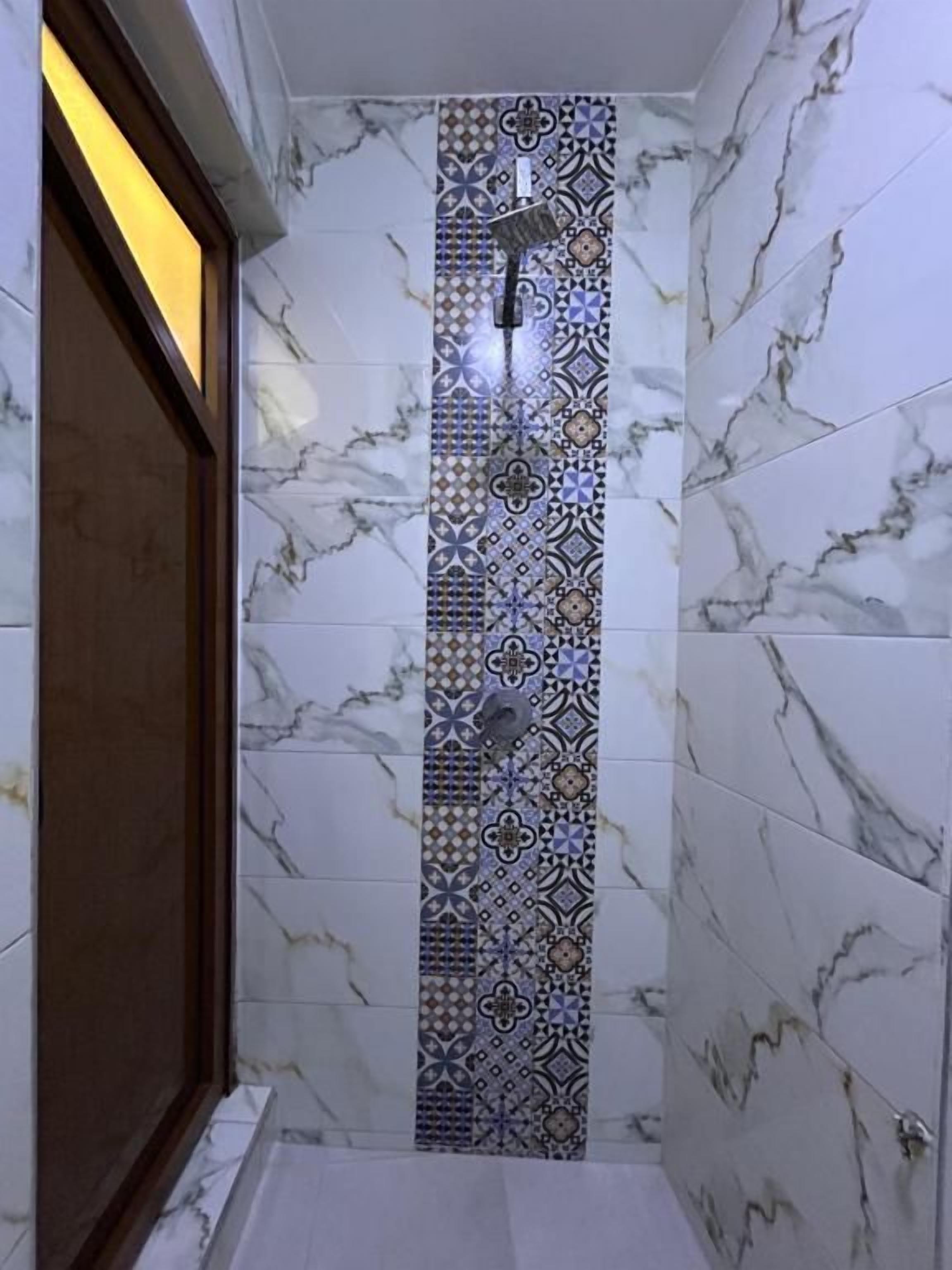 Een badkamer met een douchegedeelte, afgewerkt met een decoratief betegeld patroon en een marmeren wand.
