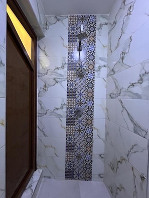 Een badkamer met een douchegedeelte, afgewerkt met een decoratief betegeld patroon en een marmeren wand.