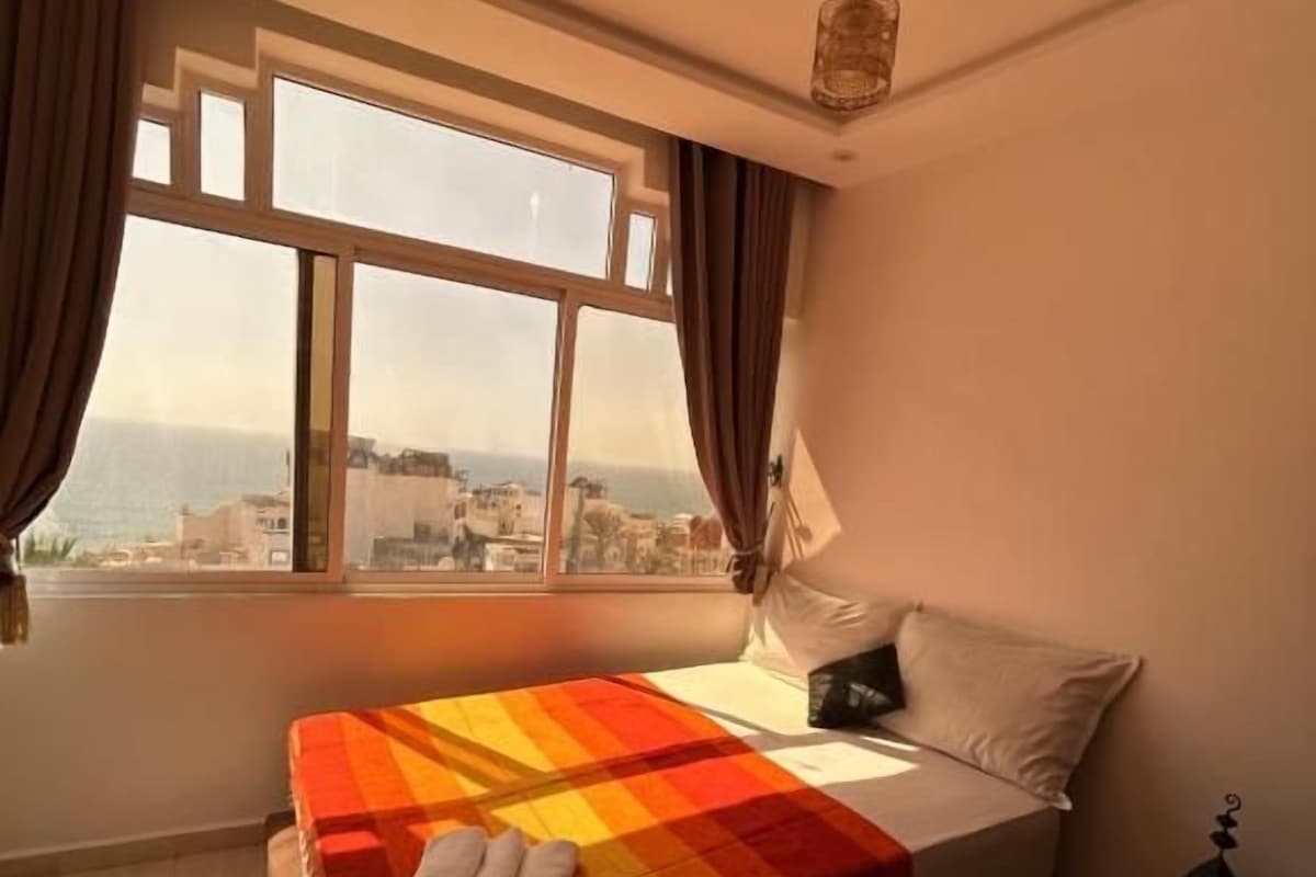 Een slaapkamer met een bed, een raam en uitzicht op gebouwen.