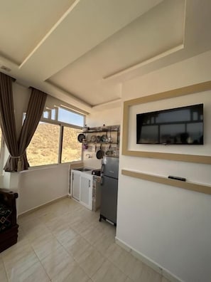 Eine kleine Küche mit Kühlschrank, Spüle und einem Fenster mit Vorhängen.