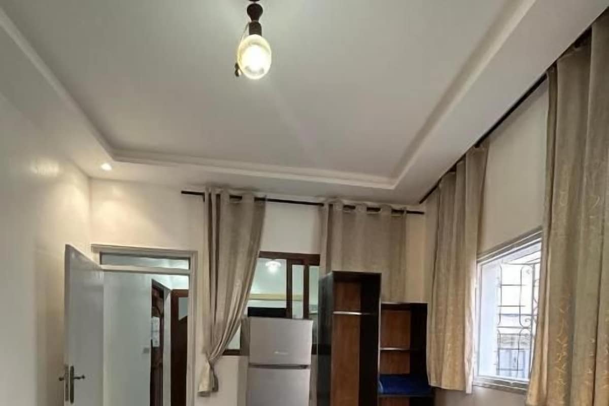 Een hotelkamer met twee bedden, een kledingkast, een koelkast en een raam met gordijnen.