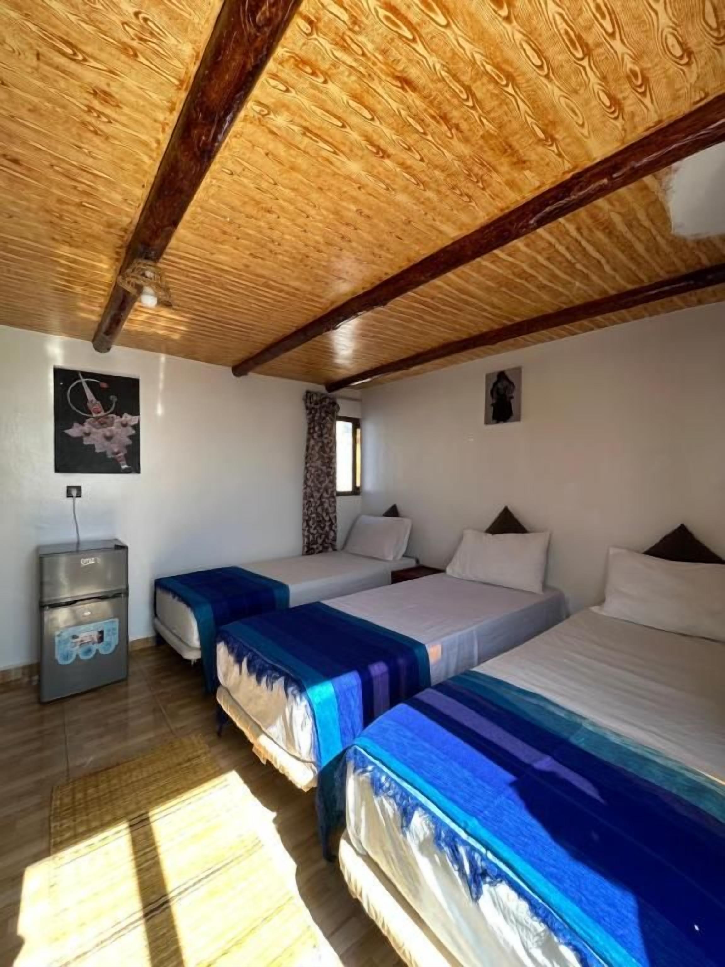 Habitación con tres camas, vigas de madera en el techo, un escritorio pequeño y una ventana.