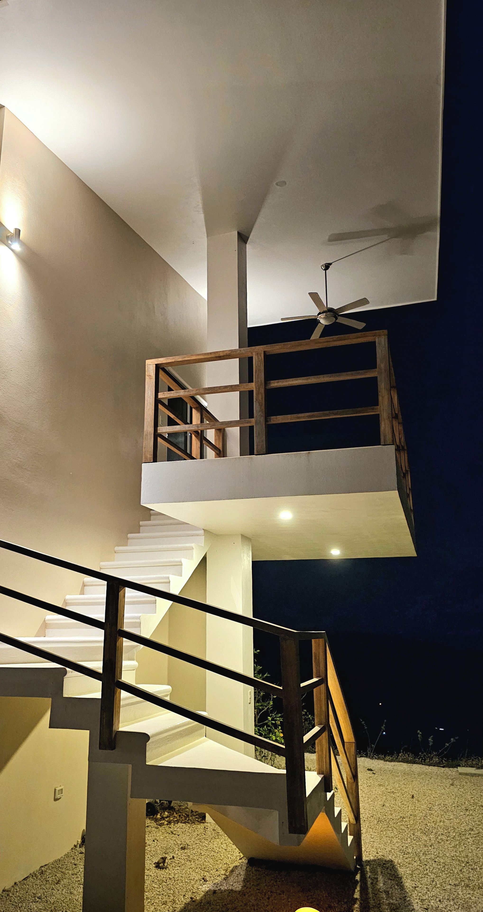 Un escalier extérieur à plusieurs niveaux, doté d’une rambarde en bois, d’un ventilateur de plafond et d’un luminaire.