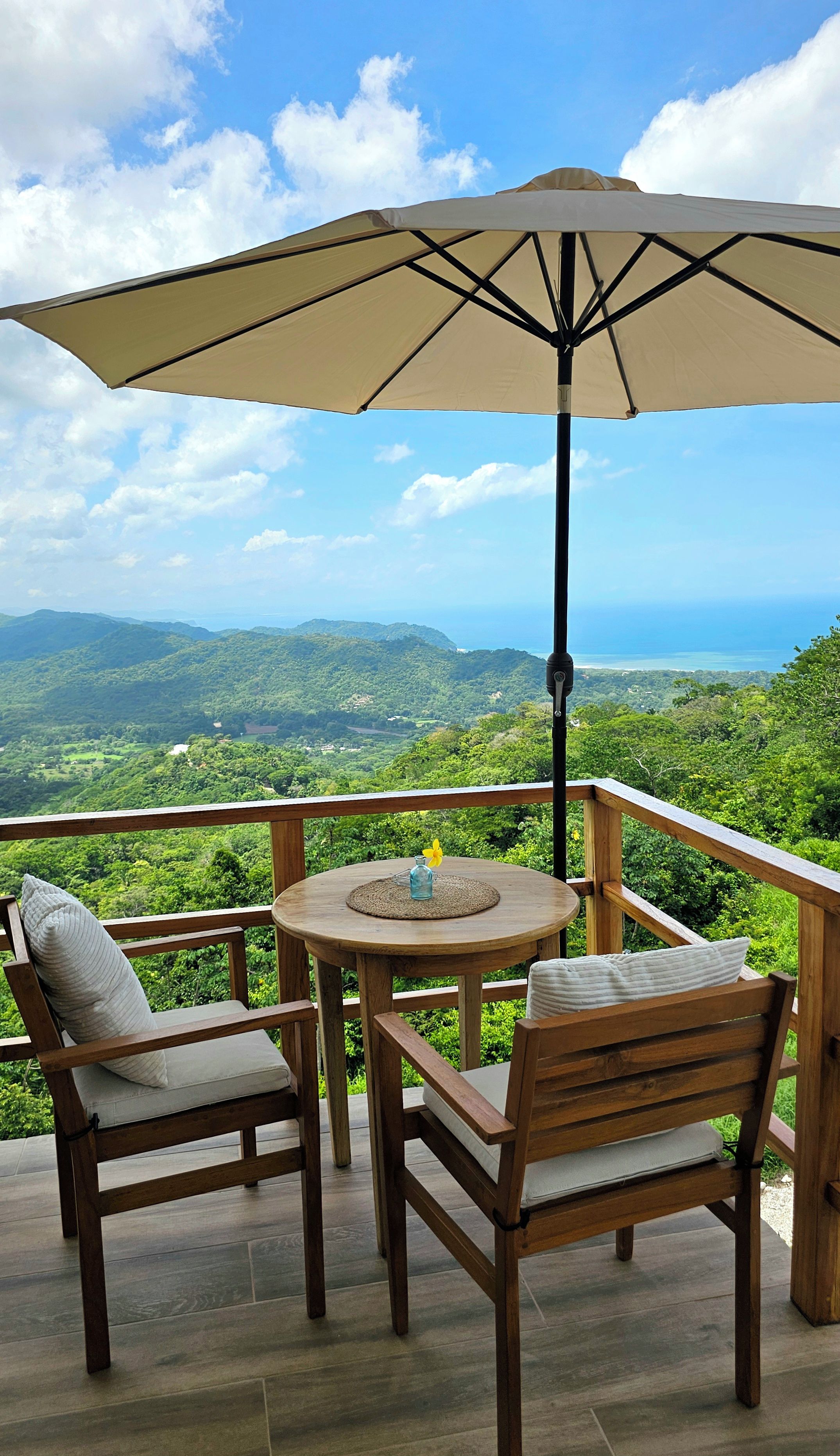A wooden deck with a table and chairs, an umbrella, and a view of a mountainous landscape.