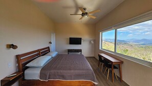 Een slaapkamer met een bed, een bureau, een televisie en een raam met uitzicht op de bergen.