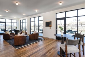 Une pièce spacieuse dotée de grandes fenêtres, d’un plancher en bois et de meubles modernes, notamment des canapés et des fauteuils.