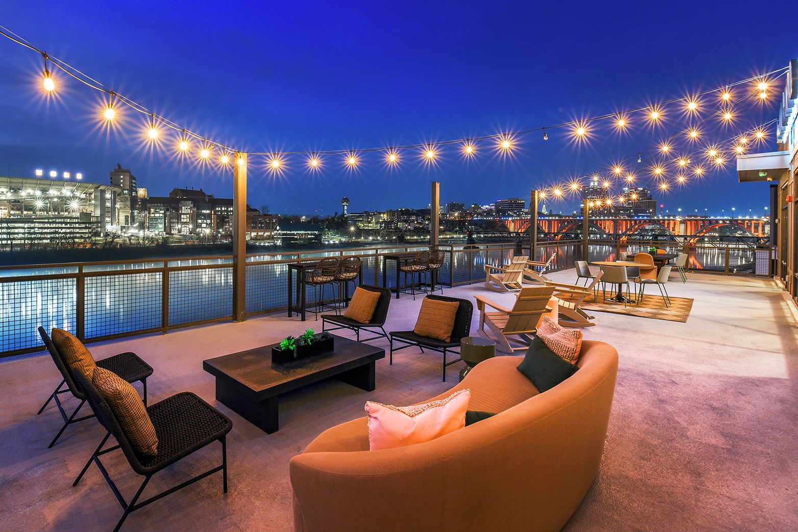 Terraza en la azotea con asientos, vistas a un paisaje urbano y luces colgantes.