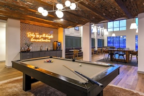 Une table de billard avec des billes, un panneau lumineux au néon et un coin bar avec des sièges.