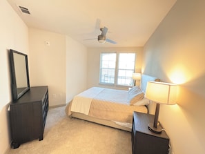 A bedroom with a bed, a dresser, a mirror, a ceiling fan, and a window. - Riverfront Knoxville Suite - Neyland Stadium Views - Pool + Parking (Knoxville)