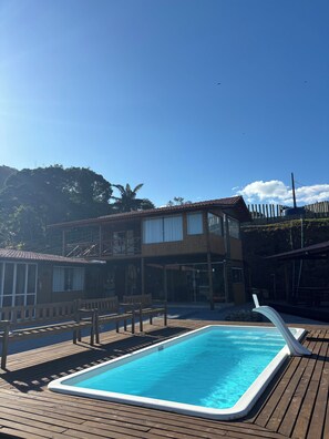 A wooden deck with a swimming pool, a two-story building with large windows, and a wooden fence.