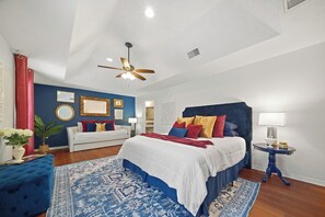 A bedroom with a large bed, a ceiling fan, a blue and white patterned rug, and a white sofa. - Reveille Roundabout: An Aggie Gathering Place 5 min from Kyle Field Sleeps 27 (Bryan)