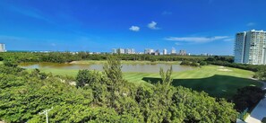 A golf course with a pond, surrounded by dense greenery and tall buildings in the background. - Relax in a Quiet and Cozy Loft in Cancún (cancun)