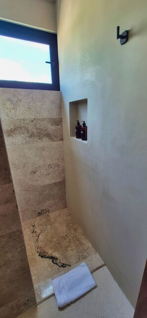 A bathroom with a shower area, a towel on the floor, and a small shelf with bottles. - Relax in a Quiet and Cozy Loft in Cancún (cancun)