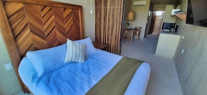 A room with a bed, a wooden headboard, a small table, and a kitchenette area. - Relax in a Quiet and Cozy Loft in Cancún (cancun)
