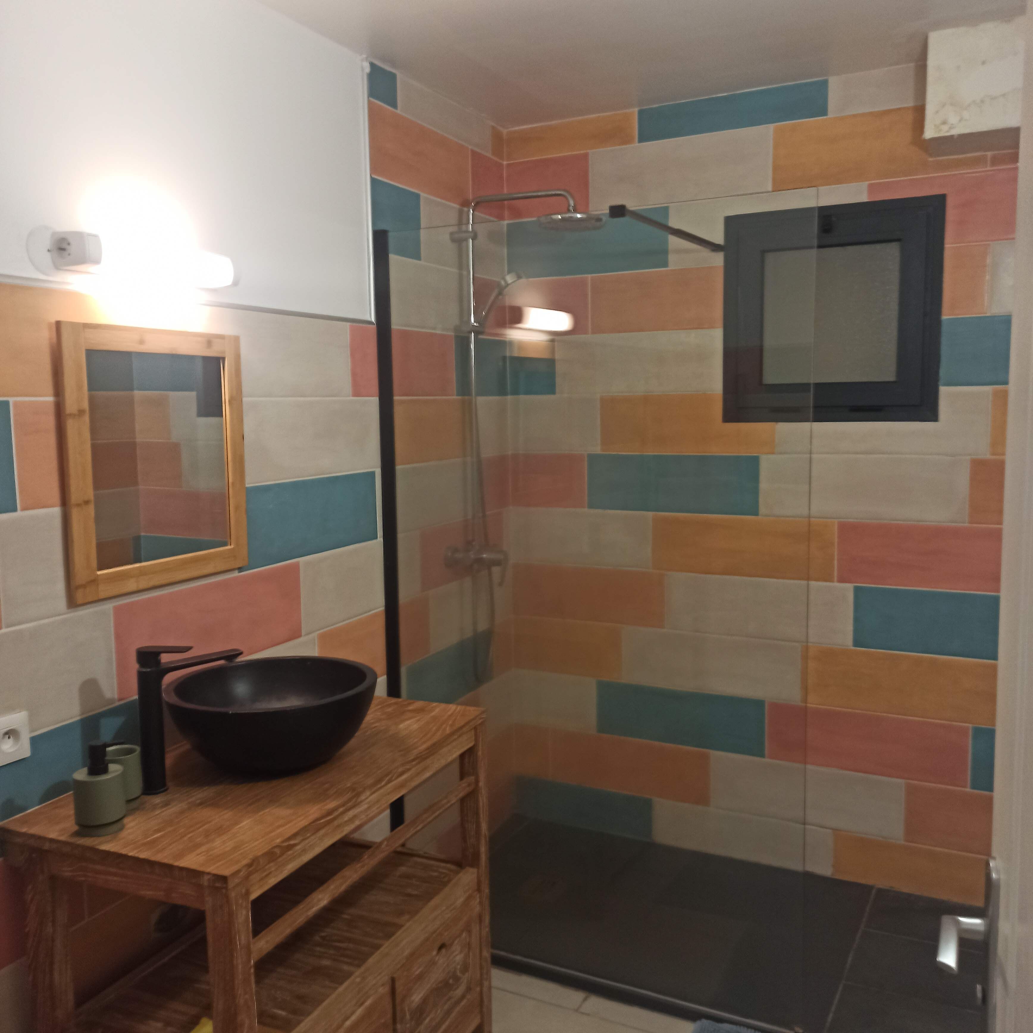 Un bagno con doccia, un mobiletto vanità in legno con lavabo nero e uno specchio.