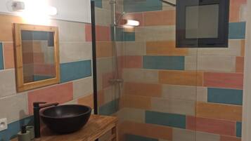 Un bagno con doccia, un mobiletto vanità in legno con lavabo nero e uno specchio.