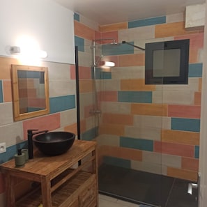 A bathroom with a shower, a wooden vanity with a black basin, and a mirror.