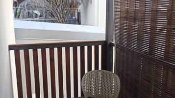 Un balcone con pavimento in legno, una sedia bianca e vista su una palma e un edificio.