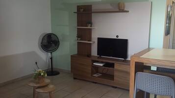 Un soggiorno con televisore, mobile TV in legno, una ventola e un tavolino con fiori.