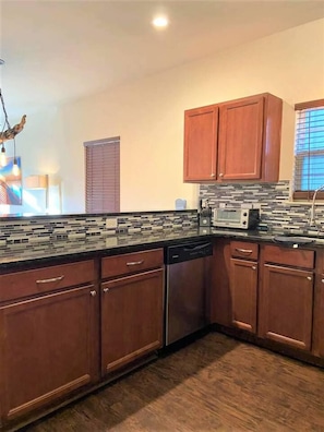 A kitchen with wooden cabinets, a microwave, and a tiled backsplash. - Cozy 3-bedroom house 5 min drive to the beach (Panama City Beach)
