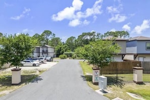 A residential driveway leading to houses with parked cars, a gated entrance, and a clear sky. - Cozy 3-bedroom house 5 min drive to the beach (Panama City Beach)