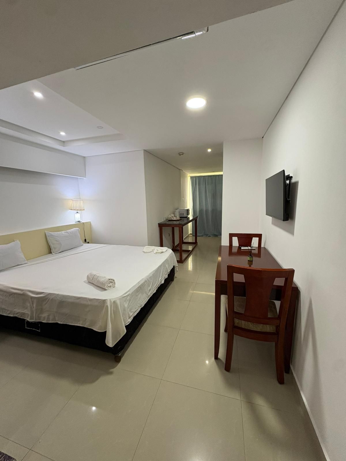 Une chambre d’hôtel comprenant un lit, un bureau, une chaise, un téléviseur fixé au mur et une fenêtre avec des rideaux.