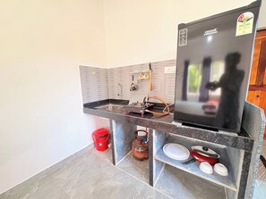 Cocina compacta con estufa a gas integrada, un refrigerador y una bombona.