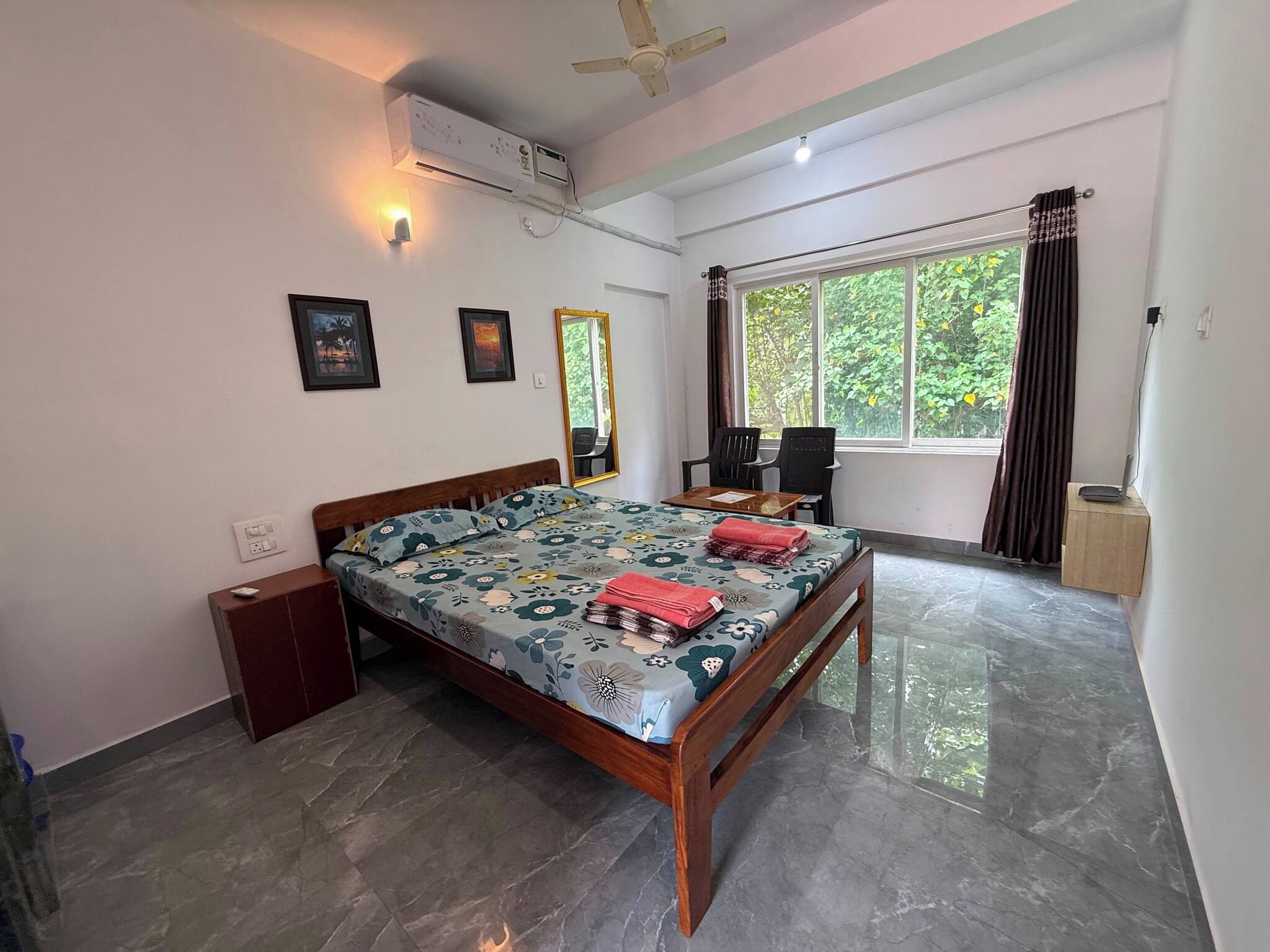 A bedroom with a bed, a desk, a chair, an air conditioning unit, and a window with curtains.
