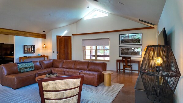A living room with a sectional sofa, a small round table, a woven chair, a lamp, and a television. - Wild Horse House - 2 bedroom, 2 bathroom house (Sedona)