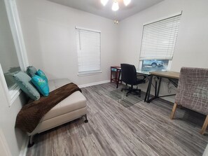 Una habitación con cama, escritorio, dos sillas y dos ventanas con persianas.