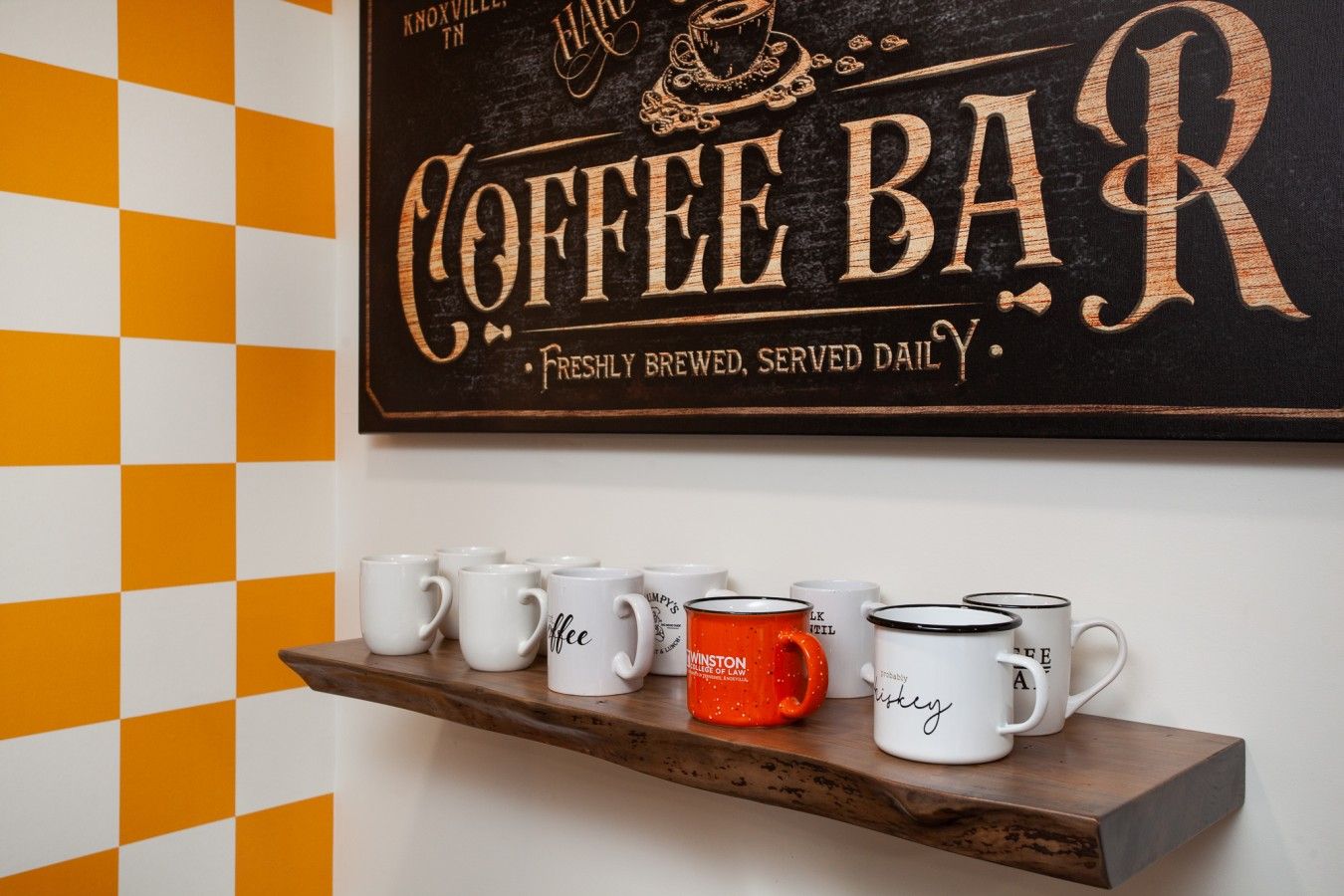 Een bordje bij een koffiebar met een houten plank eronder waarop verschillende mokken staan.