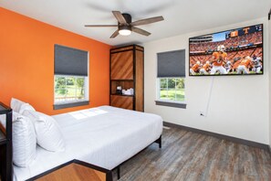 A bedroom with a bed, a ceiling fan, a TV on the wall, and a window.