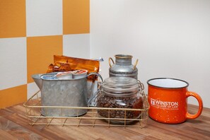 A metal container with a lid, a glass jar with a metal clasp, and an orange mug on a wooden surface.