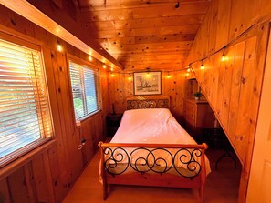 Ein Schlafzimmer einer Holzhütte mit einem Bett, einer Kommode und einem gerahmten Bild an der Wand.