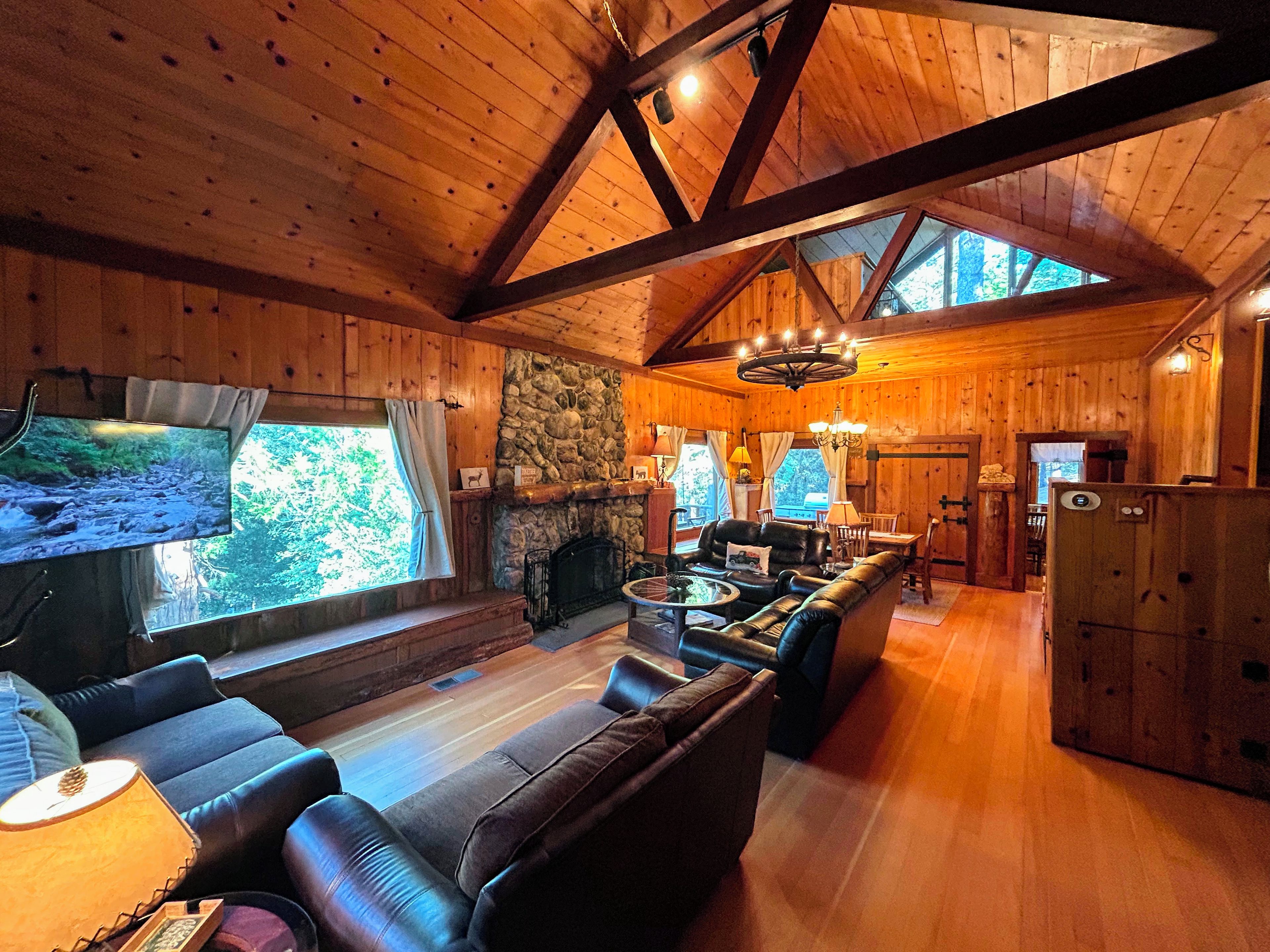 Un intérieur de chalet chaleureux avec une cheminée en pierre, des fauteuils en cuir et un téléviseur.