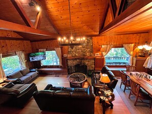 Ein gemütliches Cabin-Interieur mit Kamin aus Stein, Ledersofas, einem Holzesstisch und einem Fernseher.