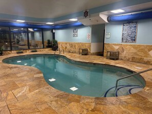 Ein Hallenbad mit klarem Wasser, einem Rettungsschwimmerstuhl und einem Hinweisschild mit Badregeln an der Wand.
