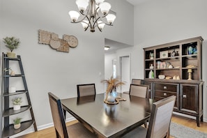 A dining area with a dark wooden table, chairs, a chandelier, a bookshelf, and decorative wall art. - Vista Verde East 207 (St. Petersburg)