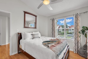 A bedroom with a bed, a ceiling fan, a window with curtains, and a view of the outside. - Vista Verde East 207 (St. Petersburg)