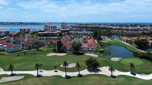 A golf course with sand bunkers and palm trees, surrounded by residential buildings and a body of water. - Vista Verde East 207 (St. Petersburg)