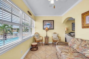 A sunlit room with a view of a pool, two wicker chairs, a sofa, and a framed picture on the wall. - Barefoot Beach Resort B201 (Indian Shores)