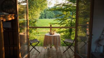 A wooden deck with a table and two chairs, overlooking a lush green landscape.