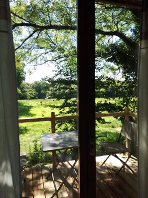 Terraza de madera con mesa y sillas, con vista a un área verde con árboles.