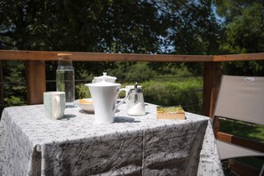 A table set outdoors with a tablecloth, a teapot, a sugar bowl, a pitcher, a glass jar, a mug, a book, and a plate with food. - Guest Room 'La Corzic' (Pléguien)